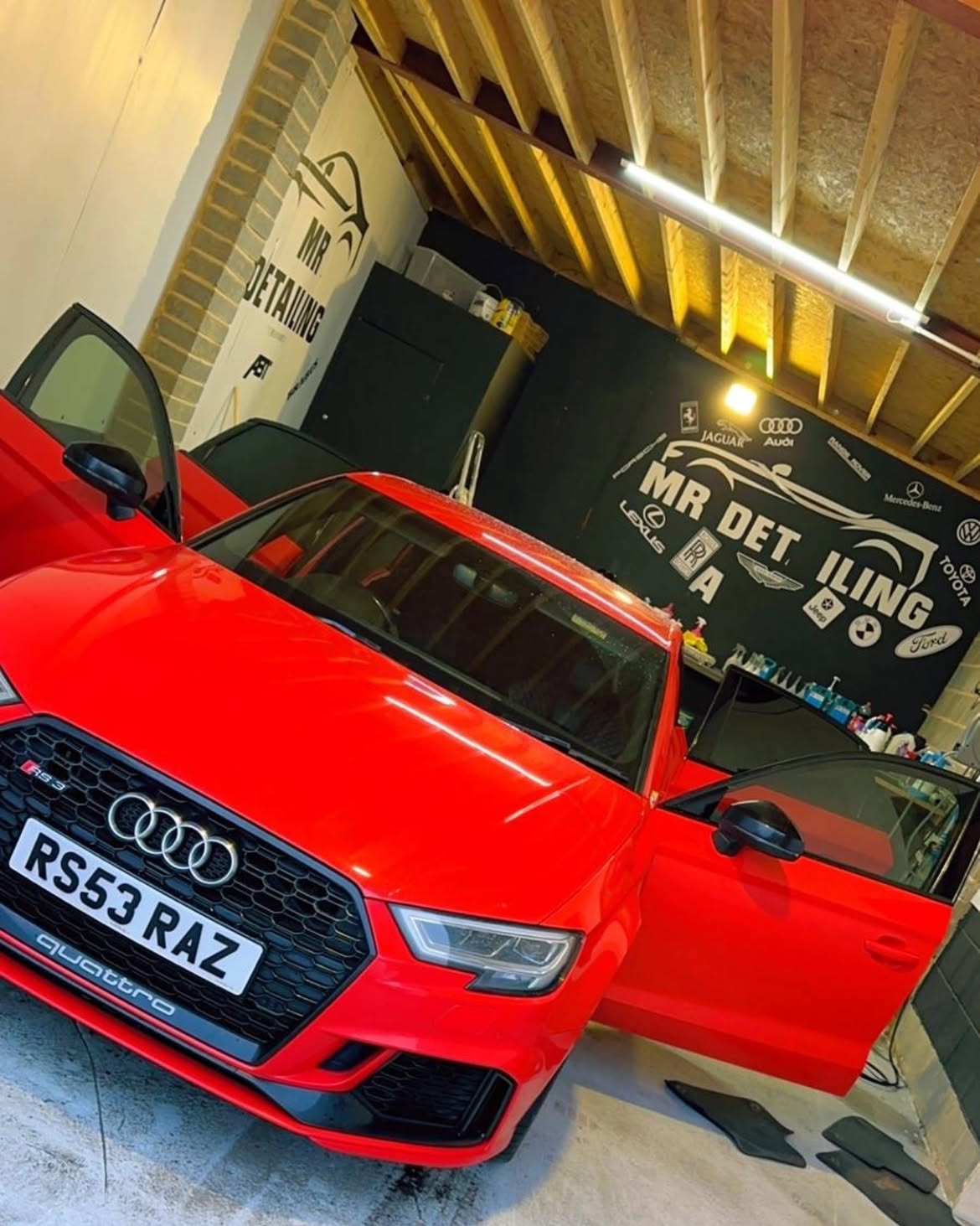 Red Audi RS3 with doors open inside the Mr Detailing workshop, marque wall behind